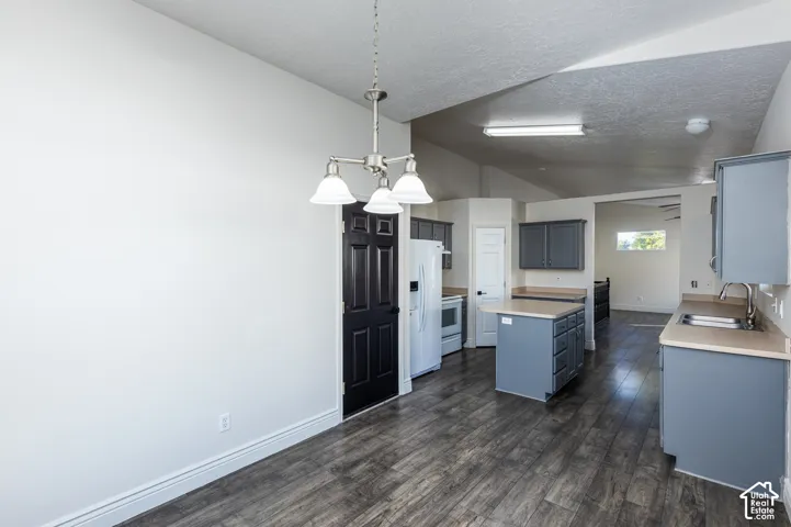 Kitchen featuring wood-finish flooring, charcoal-toned cabinetry, a center island with storage, solid-surface countertops, and a three-light pendant fixture