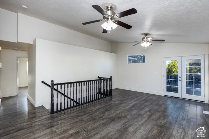 Vaulted ceilings, wood-finish flooring, two ceiling fans with integrated lighting, black spindle railing, and glass-paneled double doors