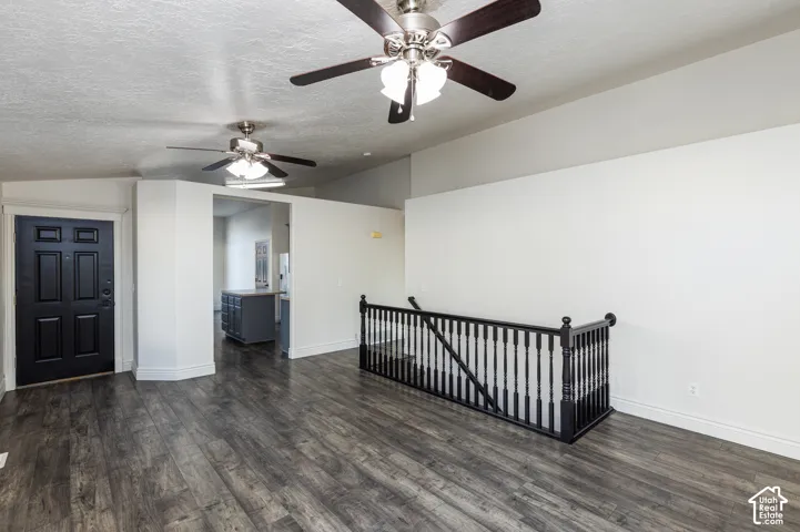 Interior space featuring wood-finish flooring, vaulted ceilings, dual ceiling fans with integrated lighting, and a staircase with a black wooden balustrade
