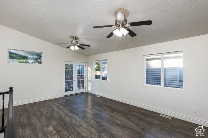 Interior space featuring vaulted ceilings, wood-finish flooring, dual ceiling fans with integrated lighting, glass-paneled double doors, and multiple windows