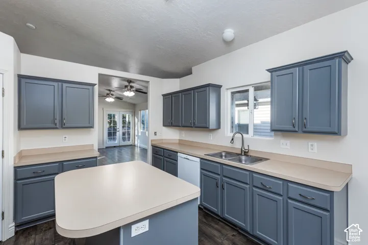 Kitchen featuring shaker-style cabinetry, solid-surface countertops, central island, double-basin stainless steel sink, and wood-finish flooring