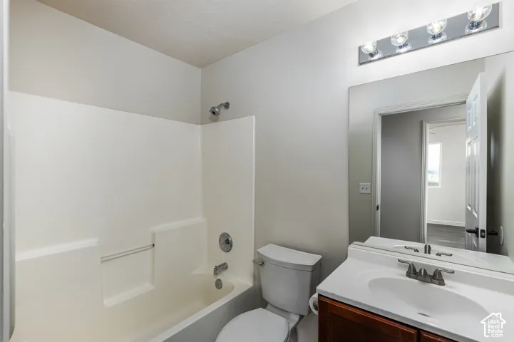 Bathroom featuring a tub-shower combination with integrated surround, a wood-finish vanity with a white countertop, and an expansive wall-mounted mirror with multi-bulb overhead lighting