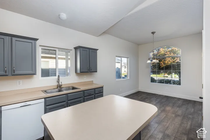 Kitchen featuring gray cabinetry, wood-finish flooring, a central island with a solid surface countertop, double-basin stainless steel sink, and a multi-pane arched window