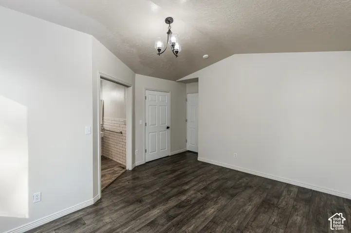 Vaulted ceilings featuring a three-light metal chandelier, wood-finish flooring, and white paneled interior doors