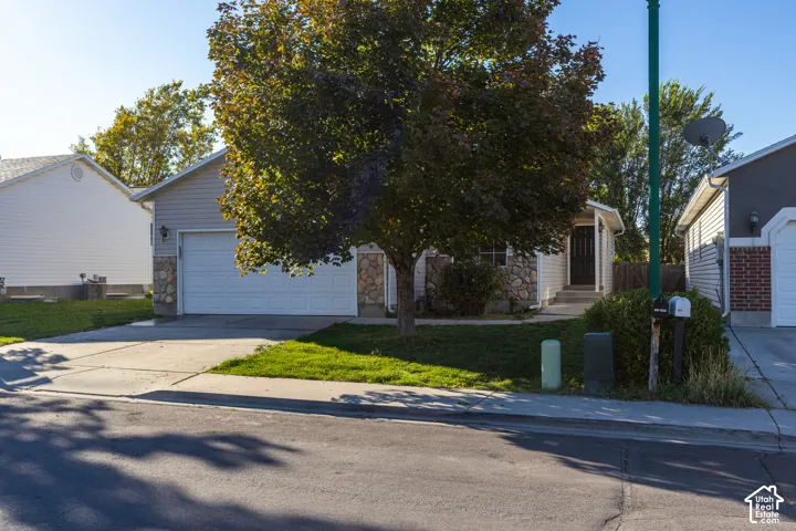Exterior facade featuring horizontal siding and stone masonry accents, concrete driveway, attached two-car garage, and mature tree-lined landscaping