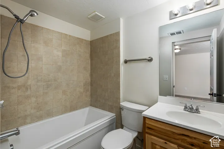Bathroom featuring a tub-shower combination with tile surround, wood-finish vanity with an integrated basin, wall-mounted mirror, and metallic light fixture