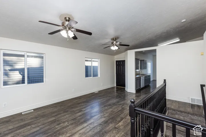 Open-concept area featuring wood-finish flooring, dual ceiling fans, sliding windows, and a dark-finished wooden staircase railing