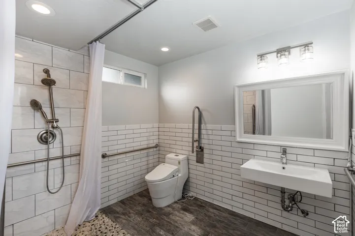 Bathroom featuring white subway tile wall accents, wood-finish flooring, a wall-mounted rectangular basin sink, and a dual-head shower system with a stone-texture floor