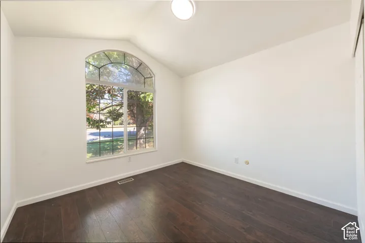Vaulted ceiling, arched window with grid detailing, and dark wood-finish flooring