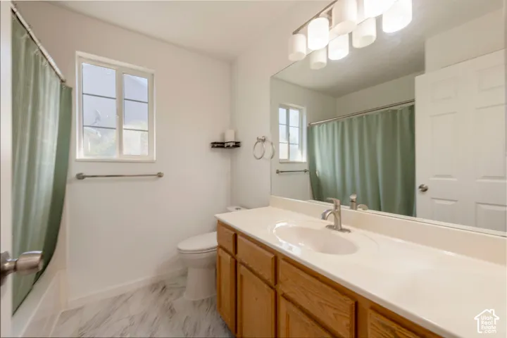 Bathroom featuring a wide vanity with a solid-surface countertop, marble-patterned tile flooring, a large wall-mounted mirror, and a multi-bulb light fixture