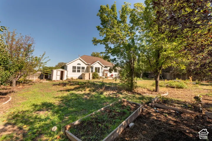 Expansive backyard featuring multiple raised garden beds, mature trees, a detached storage shed, and a fenced perimeter