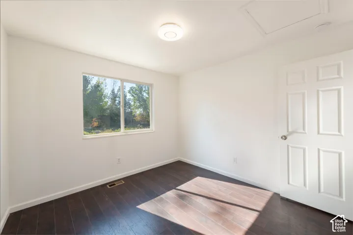 Room featuring wood-finish flooring, a six-panel door, a single-hung window, and a circular flush-mount ceiling light