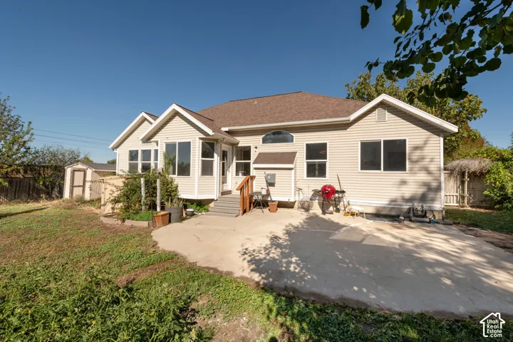 Exterior featuring light-toned vinyl siding, a concrete patio, a detached storage shed, and a gabled roofline