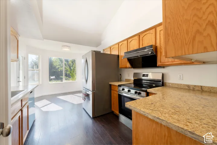 Kitchen featuring warm-tone wood cabinetry, stone-finish countertops, stainless steel appliances, wood-finish flooring, and a vaulted ceiling