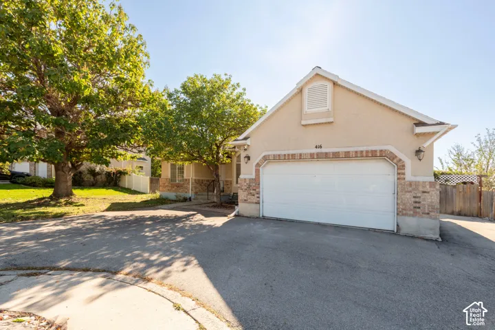 Stucco exterior featuring stone masonry accents, a gabled roofline, an attached two-car garage, and mature landscaping