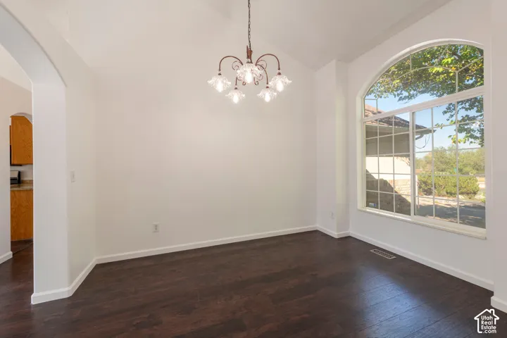Room featuring vaulted ceilings, dark wood-finish flooring, a decorative multi-arm chandelier, and a large arched window