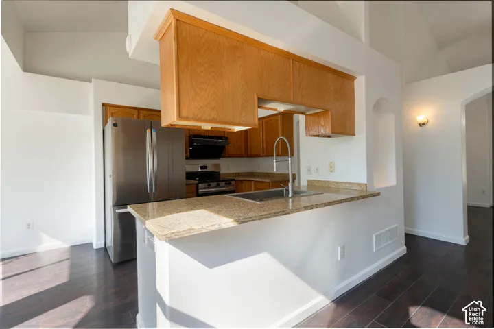Kitchen featuring wood-finish cabinetry, stone-surface countertops, stainless steel appliances, a high-arc faucet, and dark-toned flooring