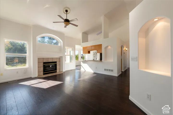 Living area featuring dark wood-finish flooring, high ceilings, fireplace with stone-finish tile surround, arched wall niches with integrated lighting, and multiple windows