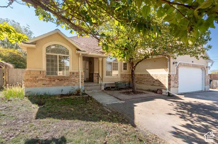 Stucco and brick facade featuring an arched window, covered entryway, and attached garage