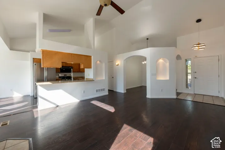 Vaulted ceilings with a ceiling fan, dark wood-finish flooring, recessed wall niches with accent lighting, architectural arched room divider, and stone-finish kitchen countertops
