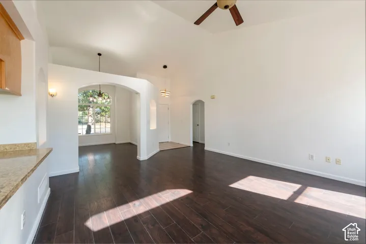 Vaulted ceilings, wood-finish flooring, arched architectural details, stone-surface countertop, and pendant lighting