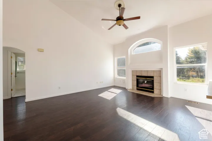 Vaulted ceilings, wood-finish flooring, a tile-surround fireplace, arched window accents, and a ceiling fan
