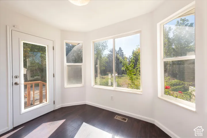 Bay window area featuring dark wood-finish flooring, a glass-paneled exterior door, and multiple windows providing natural light
