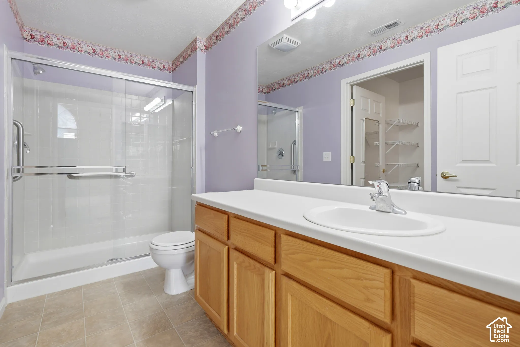 Main bathroom in main bedroom featuring a wood vanity with a white countertop, an integrated oval sink, a glass-enclosed shower with tiled surround, and a large wall-mounted mirror