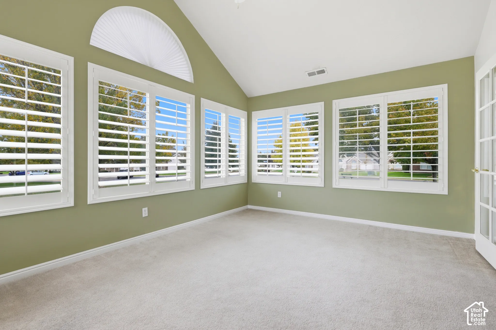 Sunroom/office space with vaulted ceiling, arched window, plantation shutters showing view of mature trees immediately out side.