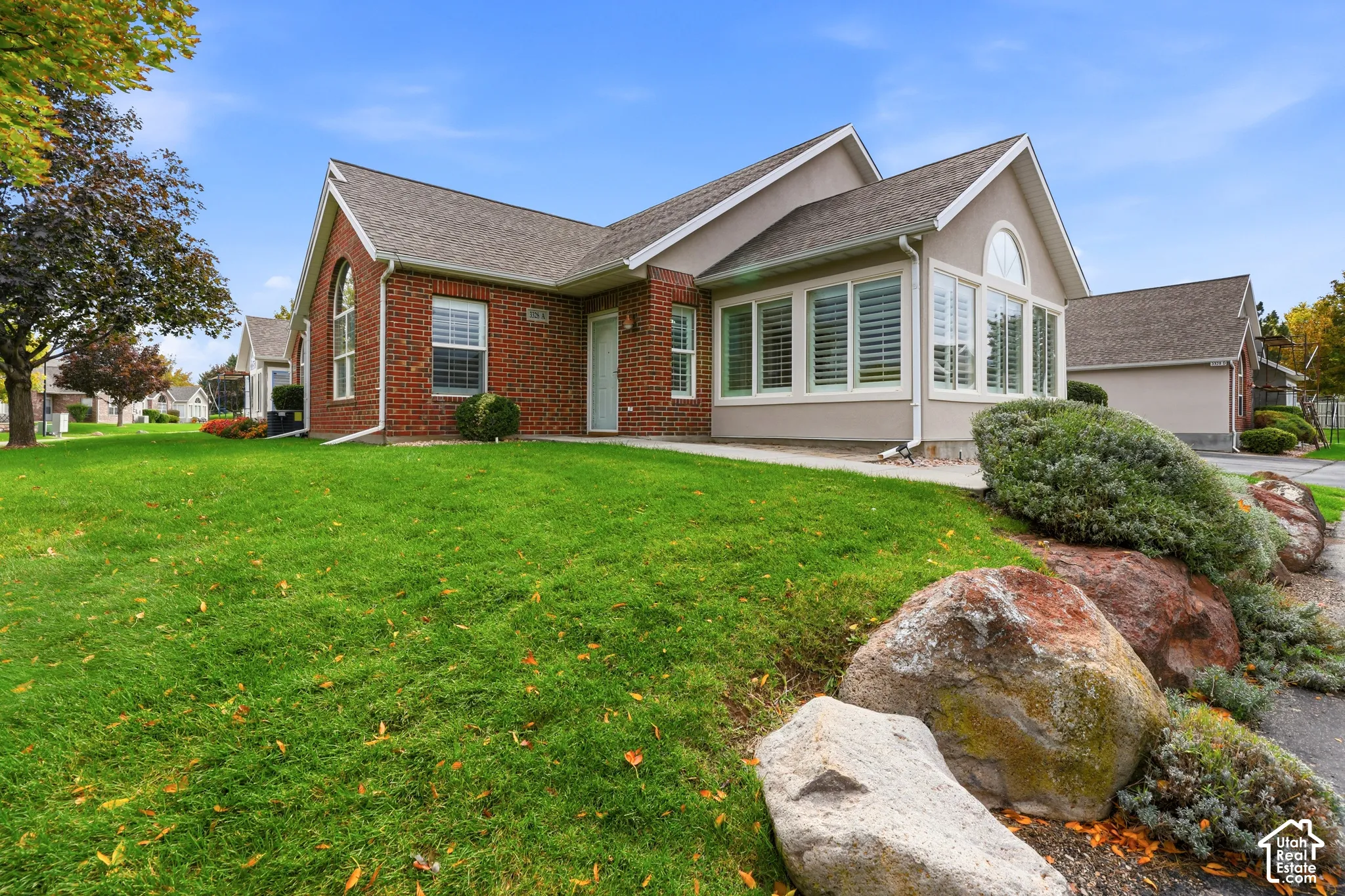 Exterior facade featuring red brick masonry and neutral siding, architectural roof shingles, arched windows, and decorative landscaping with large accent boulders