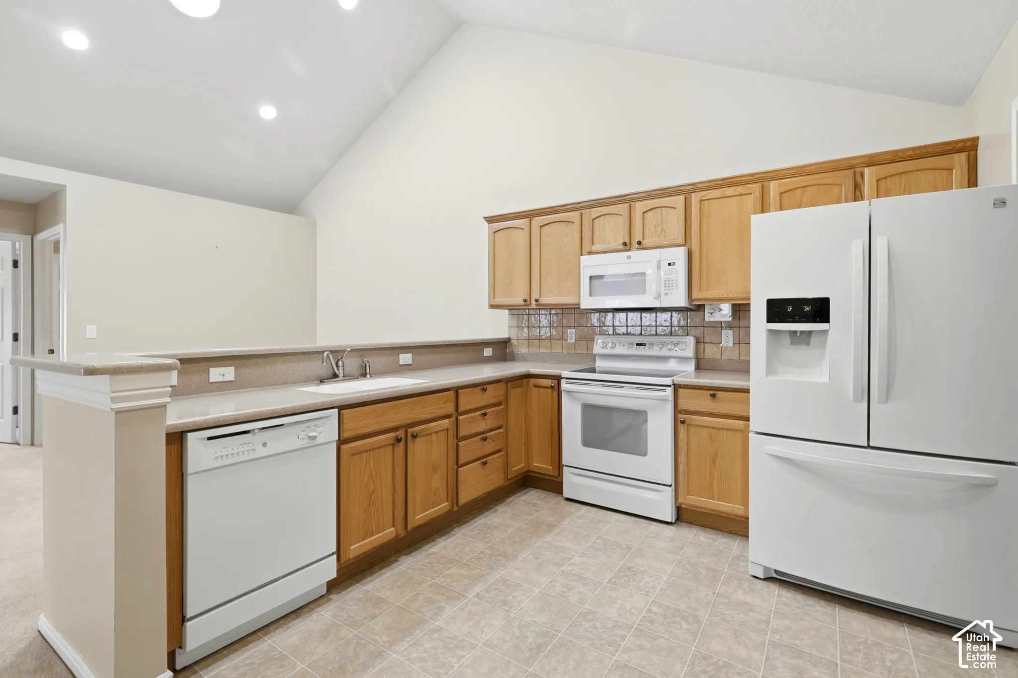 Kitchen featuring vaulted ceilings, light-toned cabinetry, solid surface countertops, tile backsplash, sky lights, and recessed lighting