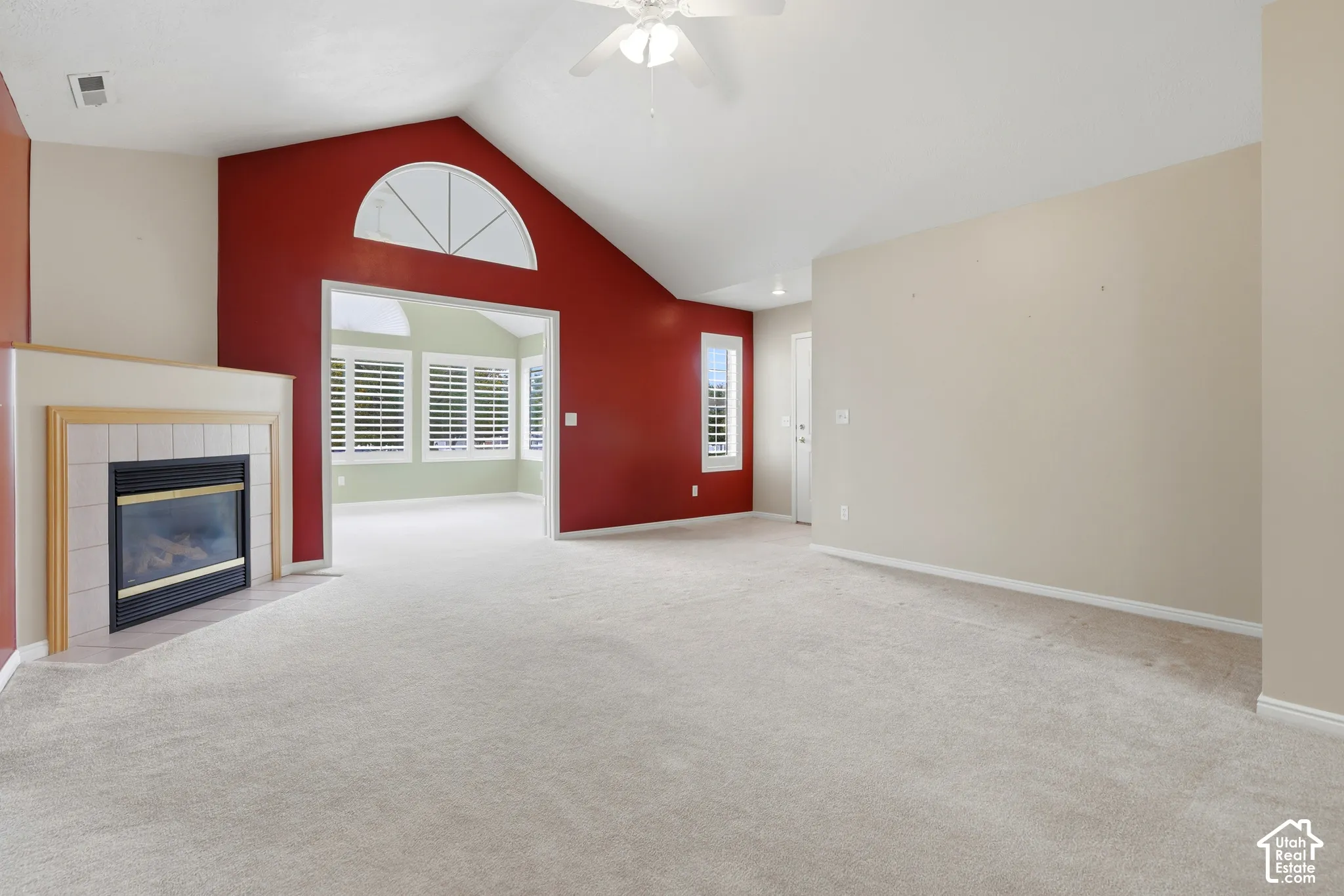 Vaulted ceiling featuring a ceiling fan, fireplace with tile surround, accent wall, and arched window