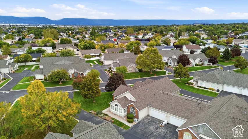 Aerial perspective featuring multi-unit structures with asphalt-shingle roofing, attached multi-car garages, and surrounding manicured green space against a mountain backdrop