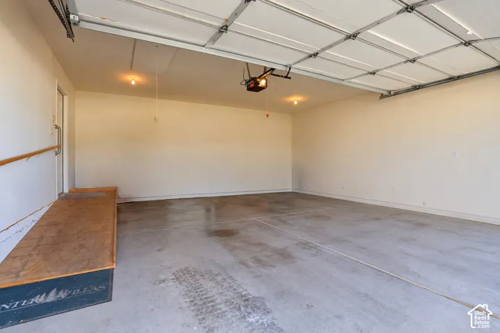 Finished garage interior featuring concrete flooring, automatic garage door opener, and a wooden ramp for easier entry with a handrail