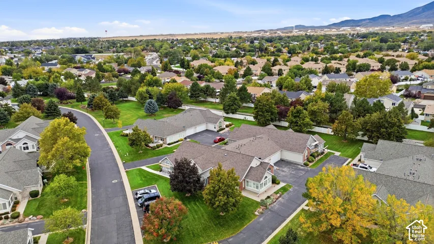 Aerial perspective featuring residential structures with asphalt shingle roofing, paved driveways, manicured green space, and mountain scenery in the distance