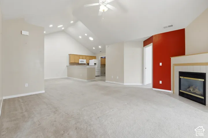 Vaulted ceilings, recessed lighting, fireplace with tile surround, ceiling fan, and kitchen breakfast bar