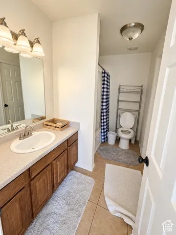 Bathroom featuring a vanity with wood-finish cabinetry, a solid surface countertop with an integrated basin, a three-light wall-mounted fixture, and tile flooring