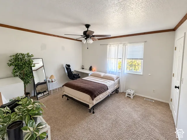 Bedroom featuring neutral wall-to-wall carpeting, ceiling fan with integrated lighting, wood crown molding, and a multi-panel interior door