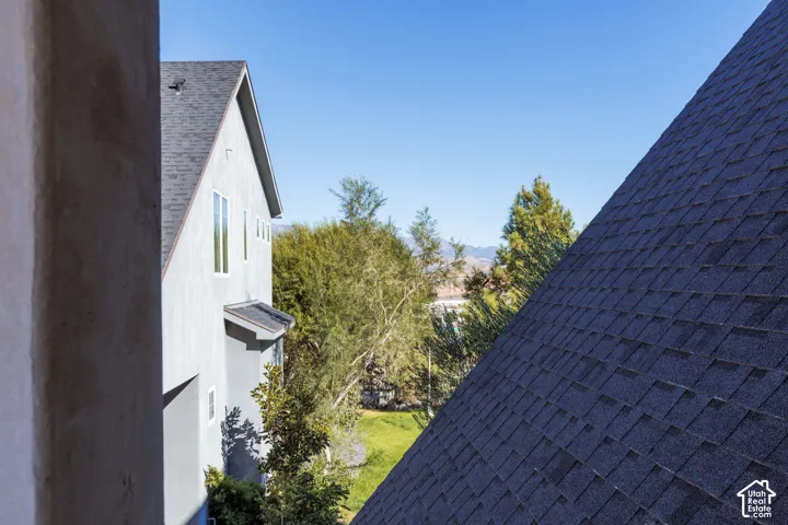 Grey stucco exterior with a multi-gabled asphalt shingle roof, vertical windows, and mature landscaping