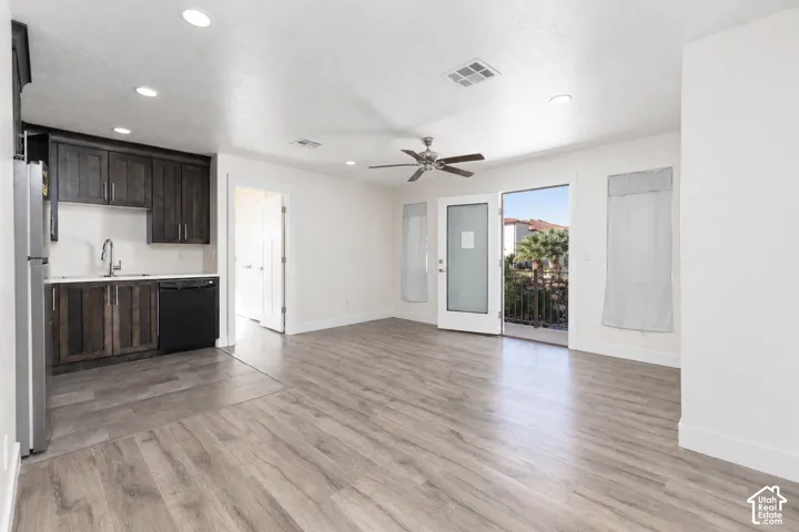 Kitchenette area featuring stained wood cabinetry, stainless steel sink, and integrated dishwasher, complemented by wood-finish flooring and recessed lighting