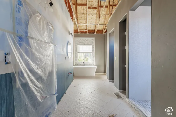 Freestanding soaking tub, herringbone-patterned floor tile, exposed vaulted wood ceiling structure, and tiled shower enclosure