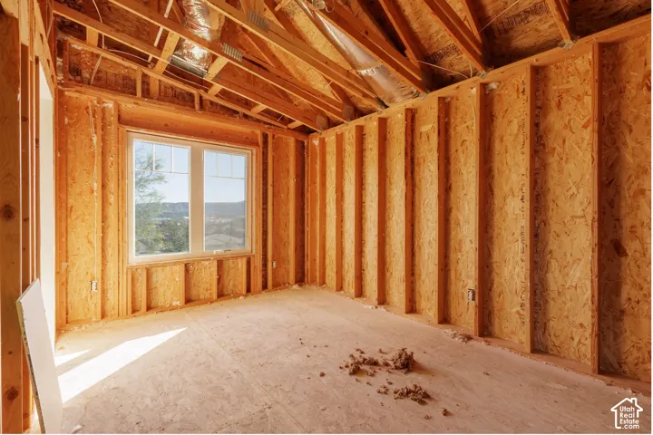 Unfinished interior space featuring exposed wood-frame construction with insulation throughout, large casement window with scenic backdrop, and concrete subfloor