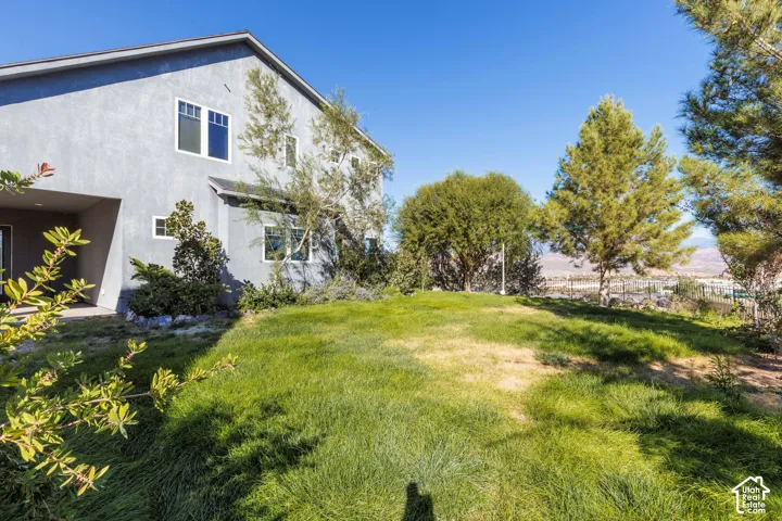 Multi-story residence featuring a stucco exterior, expansive lawn, mature trees, and a metal perimeter fence