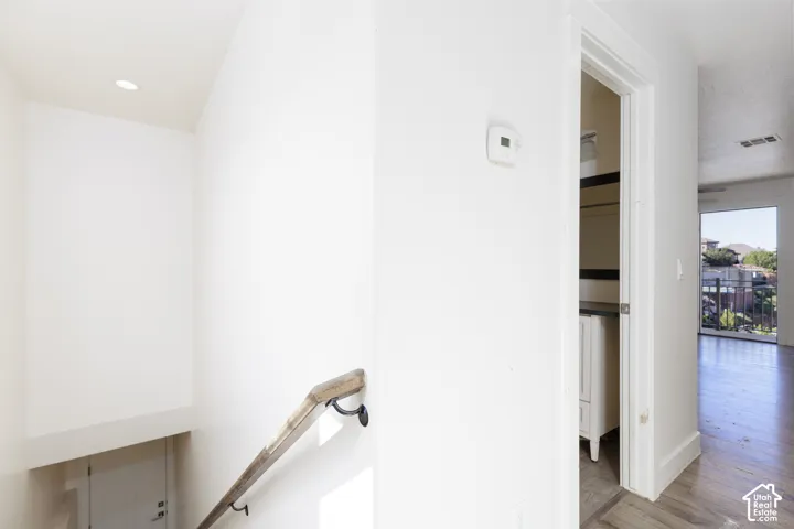 Interior hallway featuring recessed ceiling lighting, a wood-finish handrail with metal brackets, and wood-finish flooring
