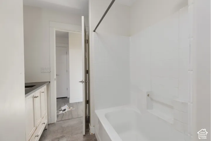 Bathroom featuring a soaking tub with integrated shower surround, white tile walls, a built-in recessed shelf, vanity with dark countertop, and wood-finish flooring