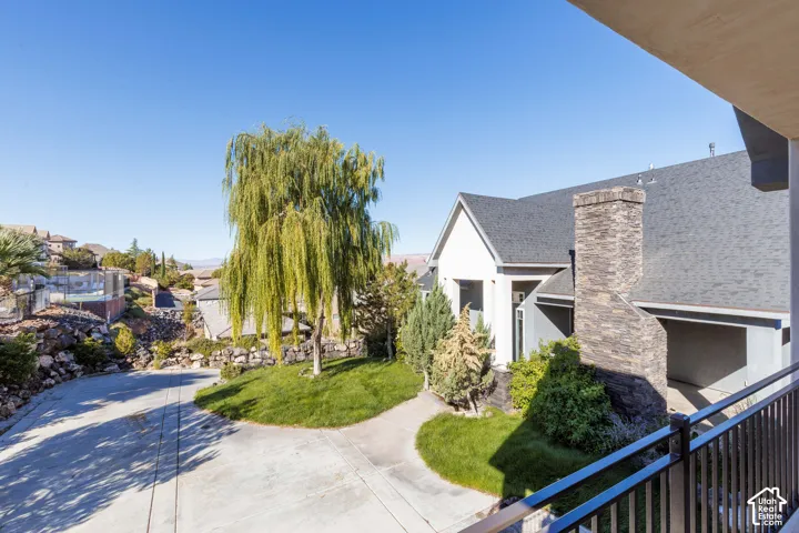 Exterior stone masonry chimney, concrete driveway, mature landscaping, and metal balcony railing