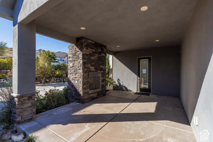 Covered patio featuring a concrete floor, stone-clad fireplace, recessed lighting, and support columns with stone detailing
