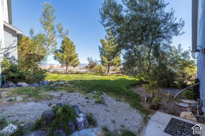 Rear yard featuring a grass lawn, gravel ground cover, rock landscaping, mature trees, and mountain backdrop