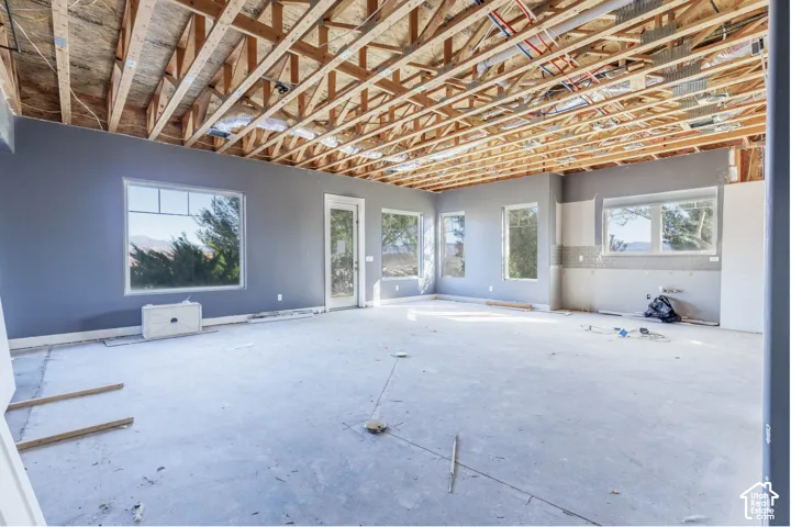 Open-concept space featuring exposed wooden truss ceiling, gray painted walls, multiple large-pane windows, and exterior glass-panel door
