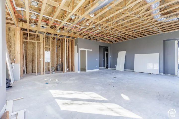 Interior space under construction featuring exposed wood roof trusses, grey-painted wall framing, and concrete slab flooring